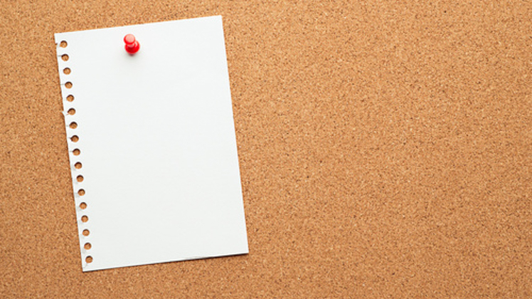 Photo of bulletin board with a blank note pinned to it. 